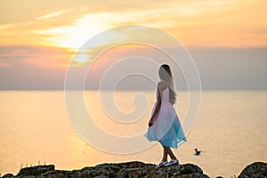 A girl at sunset looks at the sea from a high cliff.