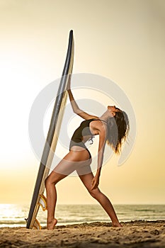Girl with surf board ready to surfing. Woman surfer holding surfboard on a beach at sunset or sunrise. Surfing at