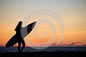 Girl with surfboard in sunset at beach