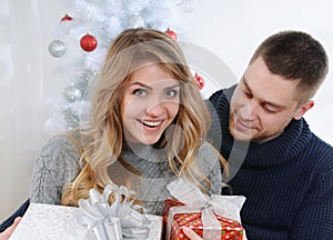 Girl surprised by her boyfriend with gifts near christmas tree