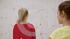 Girl surprising friend in light studio background. Two girls laughing fright at unexpected meeting on light wall