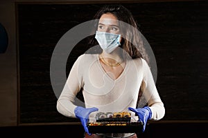 Girl with sushi. Food courier in medical mask. Delivery at quarantine coronavirus covid-19. Young woman holding 2 sushi