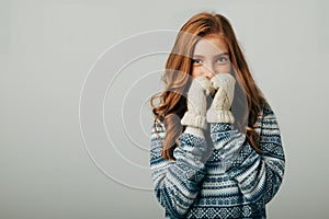 The girl in a sweater with red horns smiles, warming her face with gloves on her hands. Warm knitted gloves turned out