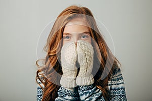 The girl in a sweater with red horns smiles, warming her face with gloves on her hands. Warm knitted gloves turned out