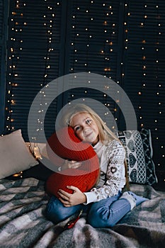 Girl in sweater sitting on bed and hugging red pillow