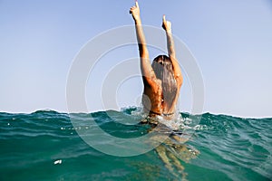 girl swim sea waves hands up splash back view
