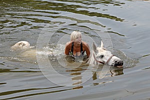 Girl swiming with her horse in summer lake