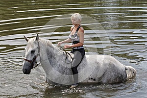 Girl swiming with her horse in summer lake