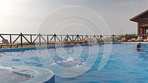 A girl with swimming goggles jumps into a pool with clear water on the background of a warm summer sunny sunset