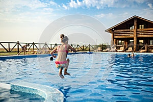 A girl with swimming goggles jumps into a pool with clear water on the background of a warm summer sunny sunset