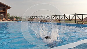 A girl with swimming goggles jumps into a pool with clear water on the background of a warm summer sunny sunset