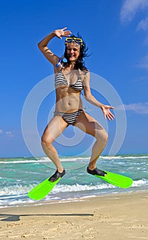 Girl in swimming mask and fins jumping at a beach photo