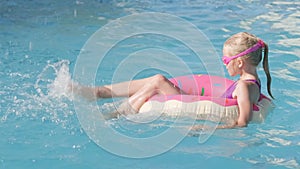 girl in swimming pool, child having fun, sitting on pink donut swimming ring, playing under water. Summer travel family