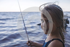 Girl in swimming wear fishing from sea beach in early morning, blue hours, active weekend, camping