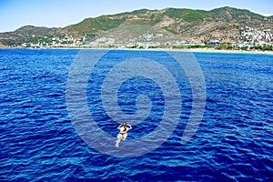 Girl swims towards the shore of Alanya Turkey being far from the coast in the sea. Woman lies on the surface of blue water