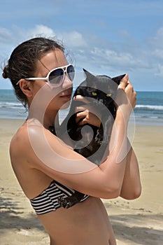 a girl in a swimsuit on the beach with a black cat