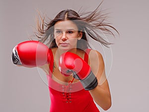 A girl in a swimsuit and boxing gloves strikes against a gray background