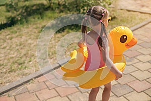 Girl in swimsuit with circle of a duck goes on way to beach to lake to swim