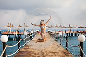 The girl in the swimsuit jumped on the pier. Happy girl on the pier. Freedom concept. The charming girl jumpping on the pier. photo