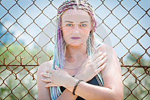 girl in a swimsuit with pigtails with sunglasses standing near a metal grate fence, portrait, hands cross to cross