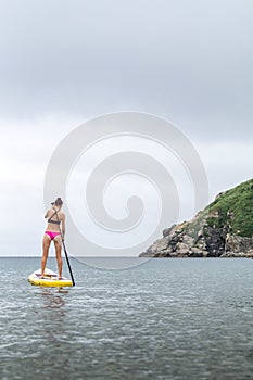 A girl in a swimsuit on a sap board paddles a paddle in the sea.