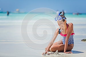 Girl in swimsuit and scuba mask sitting and having fun on tropical beach photo