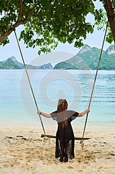 Girl swinging on a swing against the background of islands and the bay