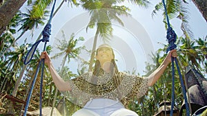 A girl swings on a swing and looks at the sunset on a tropical seashore. Freedom, rest, vacation, travel concept