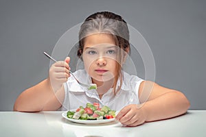 Girl at the table eating salad, overweight child.