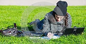 Girl with tablet, lying on green grass and writing