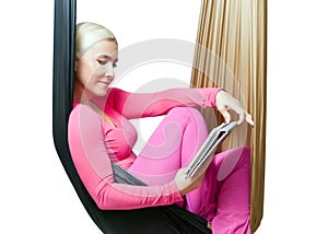 The girl with the tablet resting in the suspended hammock for yoga