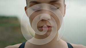 Girl take deep inhale with closed eyes meditating yoga on seashore close up.