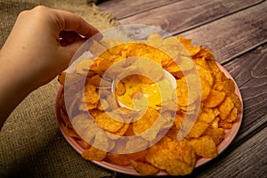The girl takes a chip from a round dish with potato chips and a saucepan with cheese sauce in the center of the plate. Close up