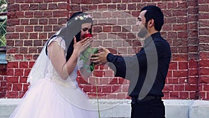 The girl takes a flower from a young man and sniffs it gently.