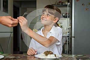 A girl takes a fork from her mother`s hand while preparing to dine at the kitchen table