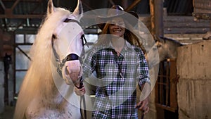 The girl takes the horse out of the stall. Portrait. The girl is smiling at the camera.