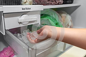 The girl takes ice from the ice maker of the freezer for cooling drinks photo