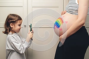 A girl takes a photograph of her pregnant mother. Expecting a child. A happy family. A girl takes a photograph of a drawing on her