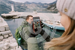 Girl takes a picture on a smartphone of guy on a pier by the sea. Side view