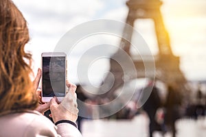 Girl takes pictures of a Eiffel Tower on a smartphone