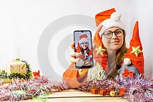 The girl takes a selfie with the Christmas gnomes. A 30-35 year old girl wearing a santa claus hat is being photographed