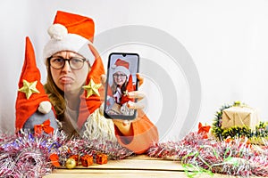 The girl takes a selfie with the Christmas gnomes. A 30-35 year old girl wearing a santa claus hat is being photographed