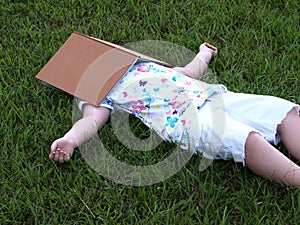 little girl lying in grass taking break under book