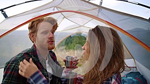 Girl taking care about guy hair in camping tent. Couple drinking tea from mugs