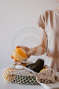 The girl is taking an orange from an eco-aware handbag with a variety of fruit