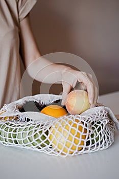 The girl is taking a peach from an eco-aware handbag with a variety of fruits.