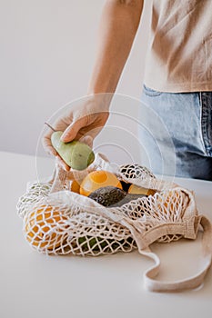 The girl is is taking a pear from an eco-aware handbag with a variety of fruits.