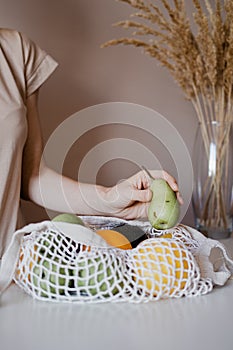 The girl is taking a pear from an eco-aware handbag with a variety of fruits.