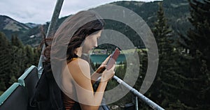 Girl taking a photo on the camera while rising up on the lift. Beautiful brunette travelling in Austria. Young woman