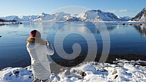 Girl taking a photo of sunny winter fjord at Lofoten archipelago at the nothern Norway